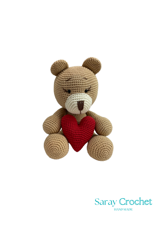 A crochet teddy bear with a red heart, possibly representing a gift for Valentine's Day or a similar occasion.
